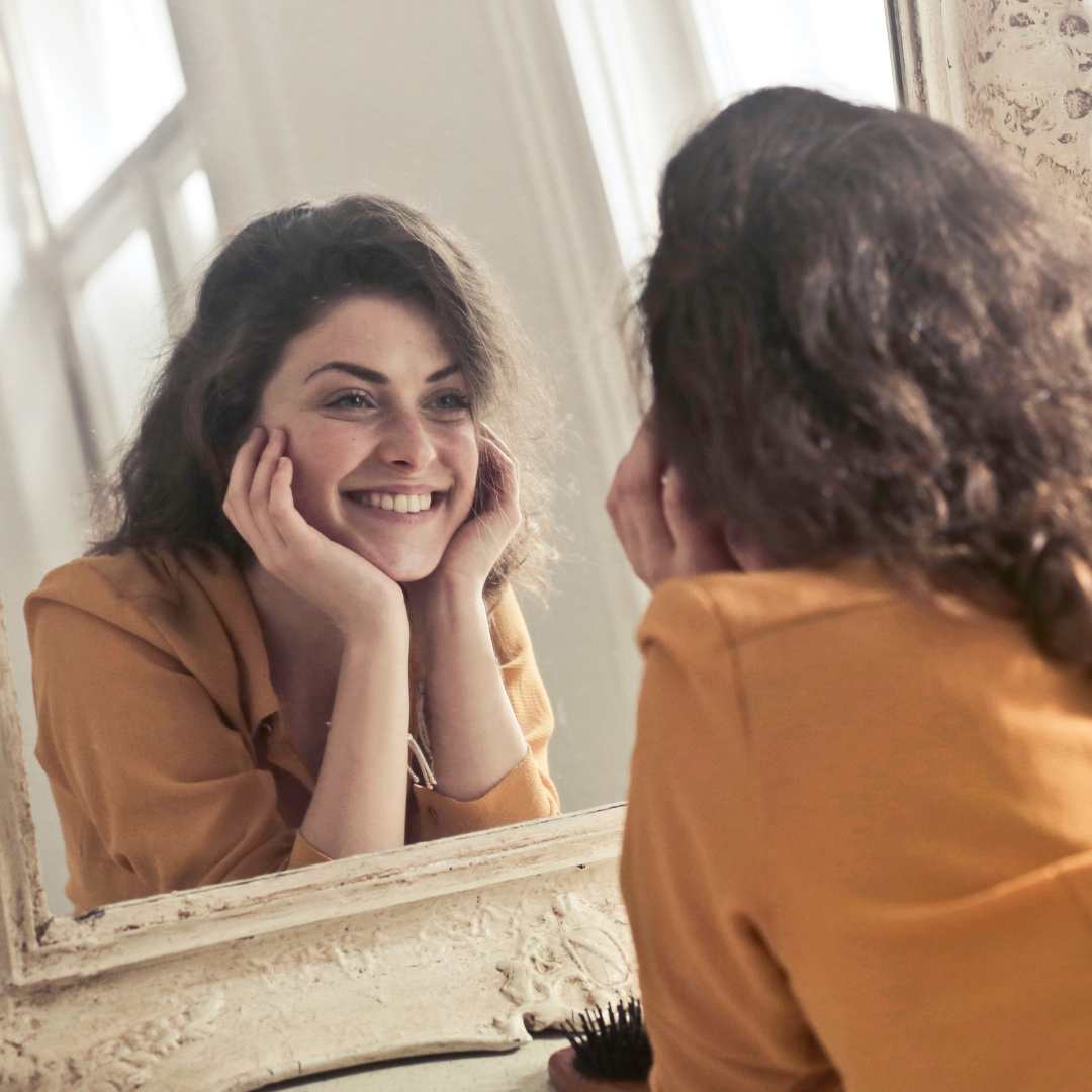 Mujer sonriendo frente al espejo reflejando confianza y bienestar gracias al ayuno intermitente