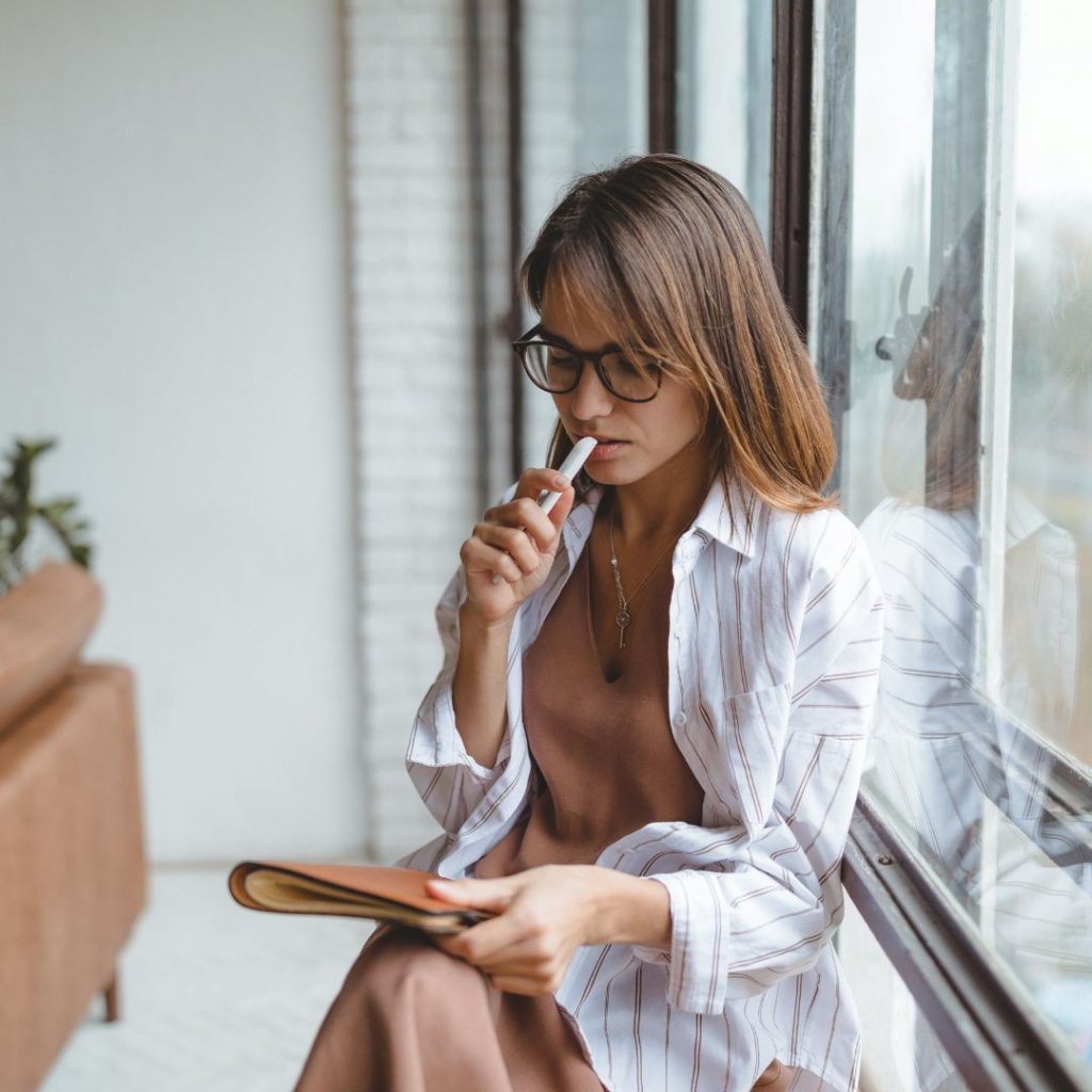 Mujer pensativa junto a una ventana con cuaderno