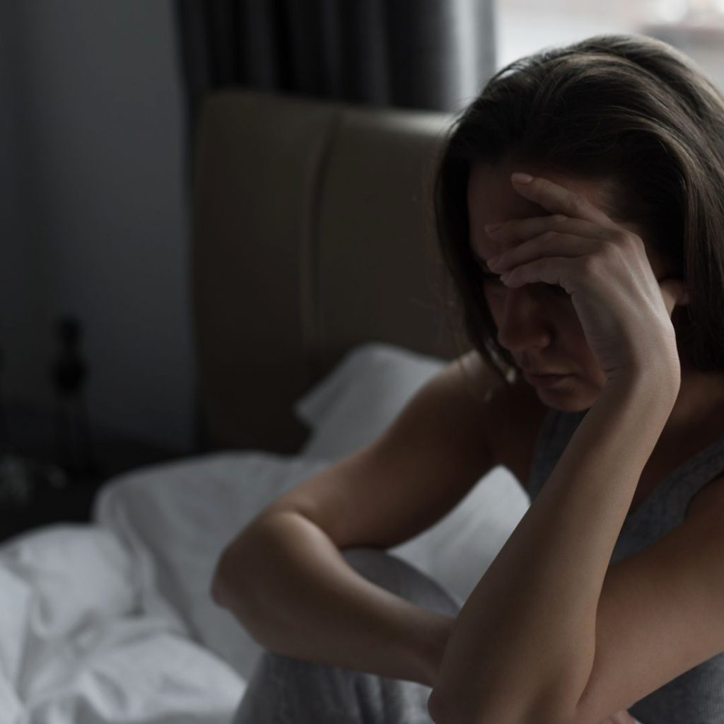 Mujer sentada en la cama con gesto de cansancio o frustración